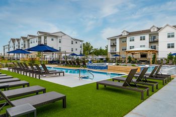A swimming pool surrounded by lounge chairs and umbrellas in front of apartment buildings.